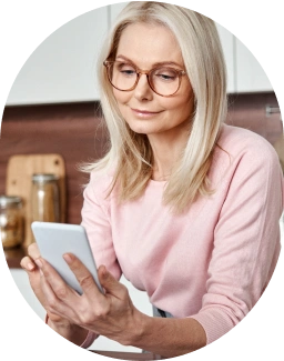 Blonde woman sitting in a kitchen, smiling, while holding a mobile phone